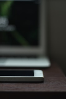 A sleek smartphone displayed on a wooden table with a blurred background of tech accessories.