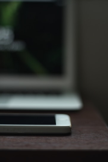 A sleek smartphone displayed on a wooden table with a blurred background of tech accessories.