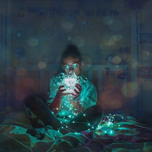 person holding green string LED light sitting on bed sheet