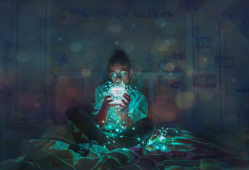 person holding green string LED light sitting on bed sheet