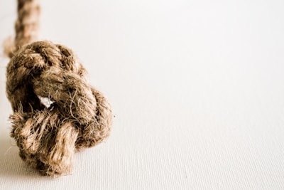 A close-up of a thick, coarse rope tied into a knot, positioned against a plain, light-colored background. The fiber texture of the rope is prominently visible, highlighting its ruggedness.