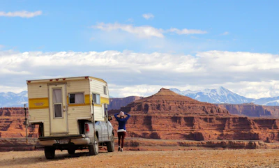 A bright red pickup truck loaded with camping gear, set against a scenic mountain backdrop.