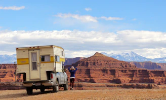 A bright red pickup truck loaded with camping gear, set against a scenic mountain backdrop.