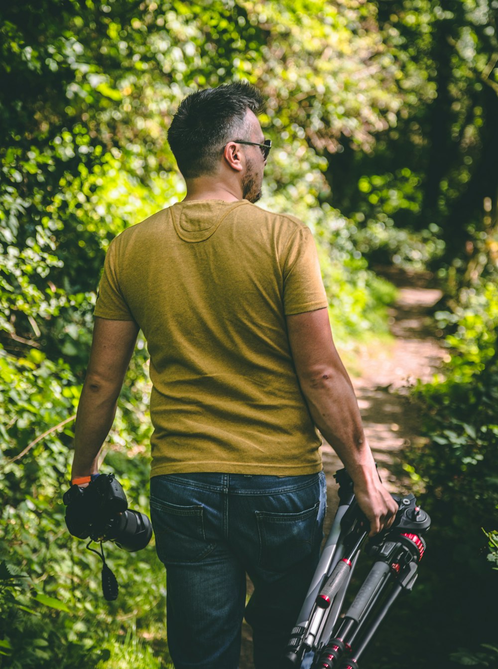 man wearing yellow T-shirt holding tripod and DSLR camera