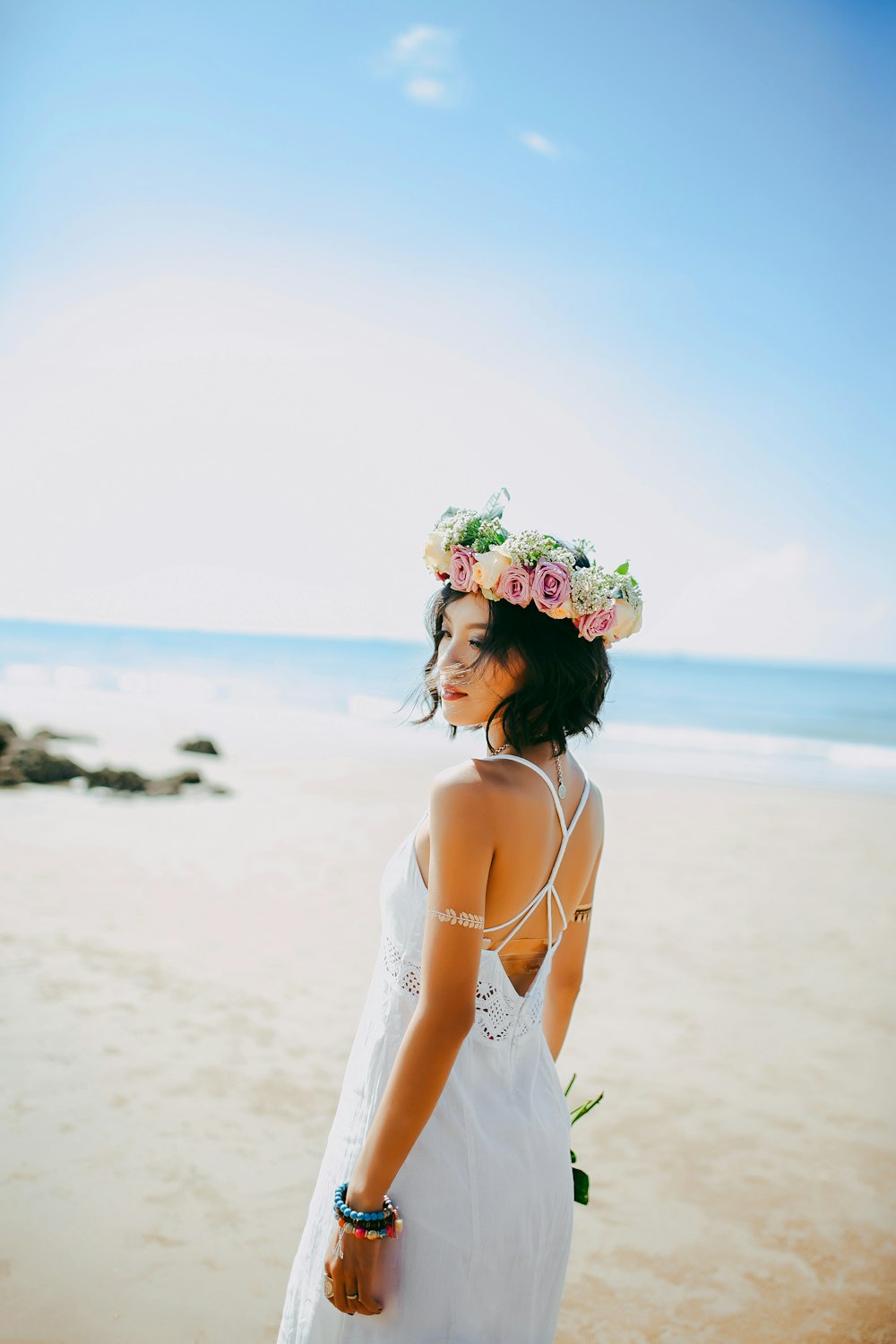 흰색 스파게티 스트랩 드레스를 입은 여자가 낮 사진 촬영 중 해변에 서 있습니다.