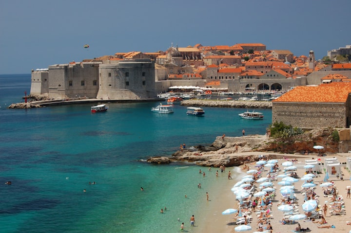 People enjoying a sunny day at a Mediterranean beach near historic European buildings