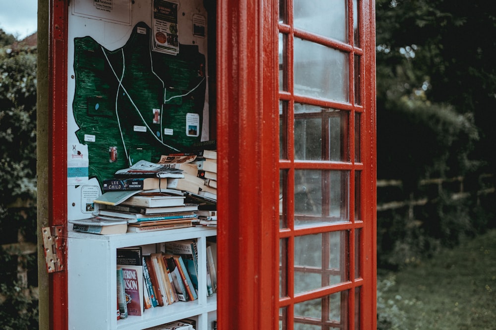 red telephone booth with book shelves beside of brick wall during daytime