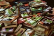 A large pile of various books, mostly paperbacks, in different colors and sizes. Many books have clearance sale stickers on them. The books are stacked haphazardly, overlapping each other. Some titles and covers are clearly visible while others are partially obscured.