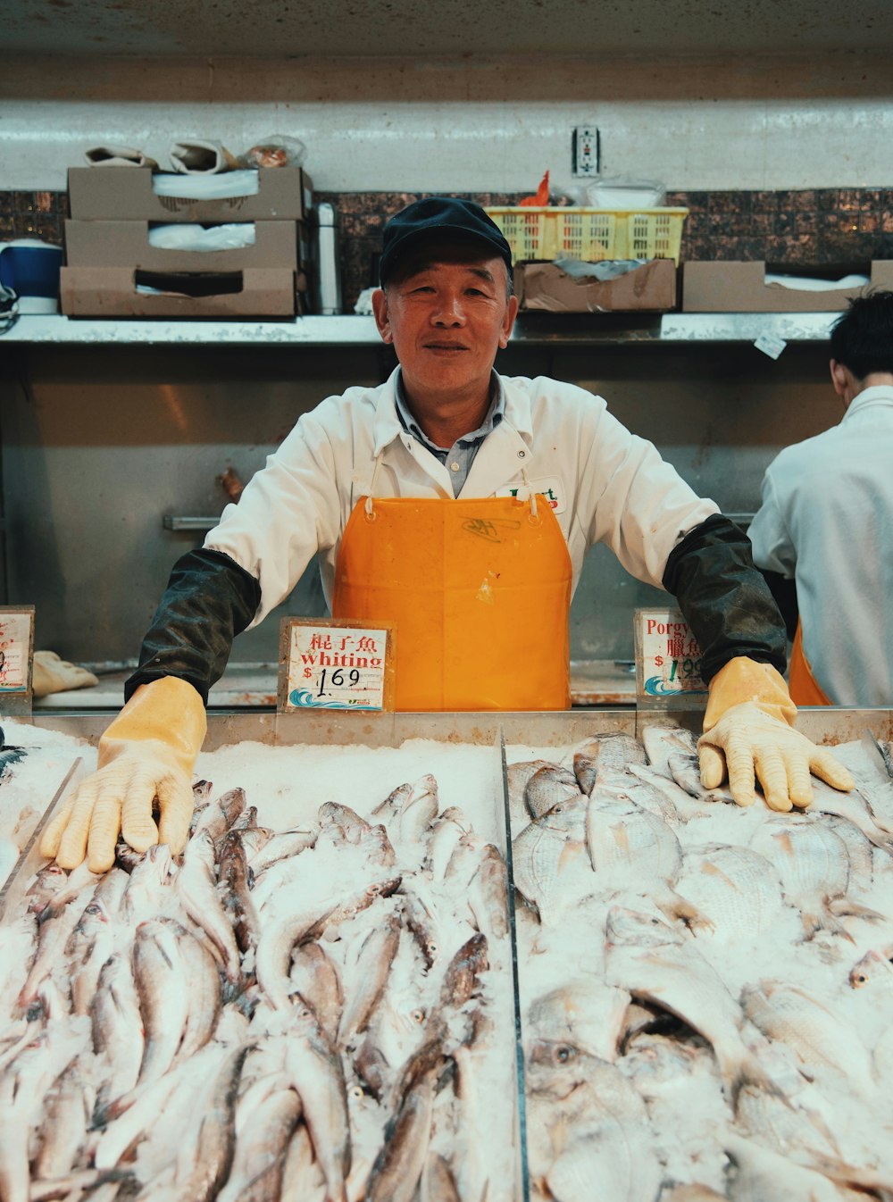 Mann mit weißem Polohemd und brauner Schürze steht in der Nähe von Fischständen