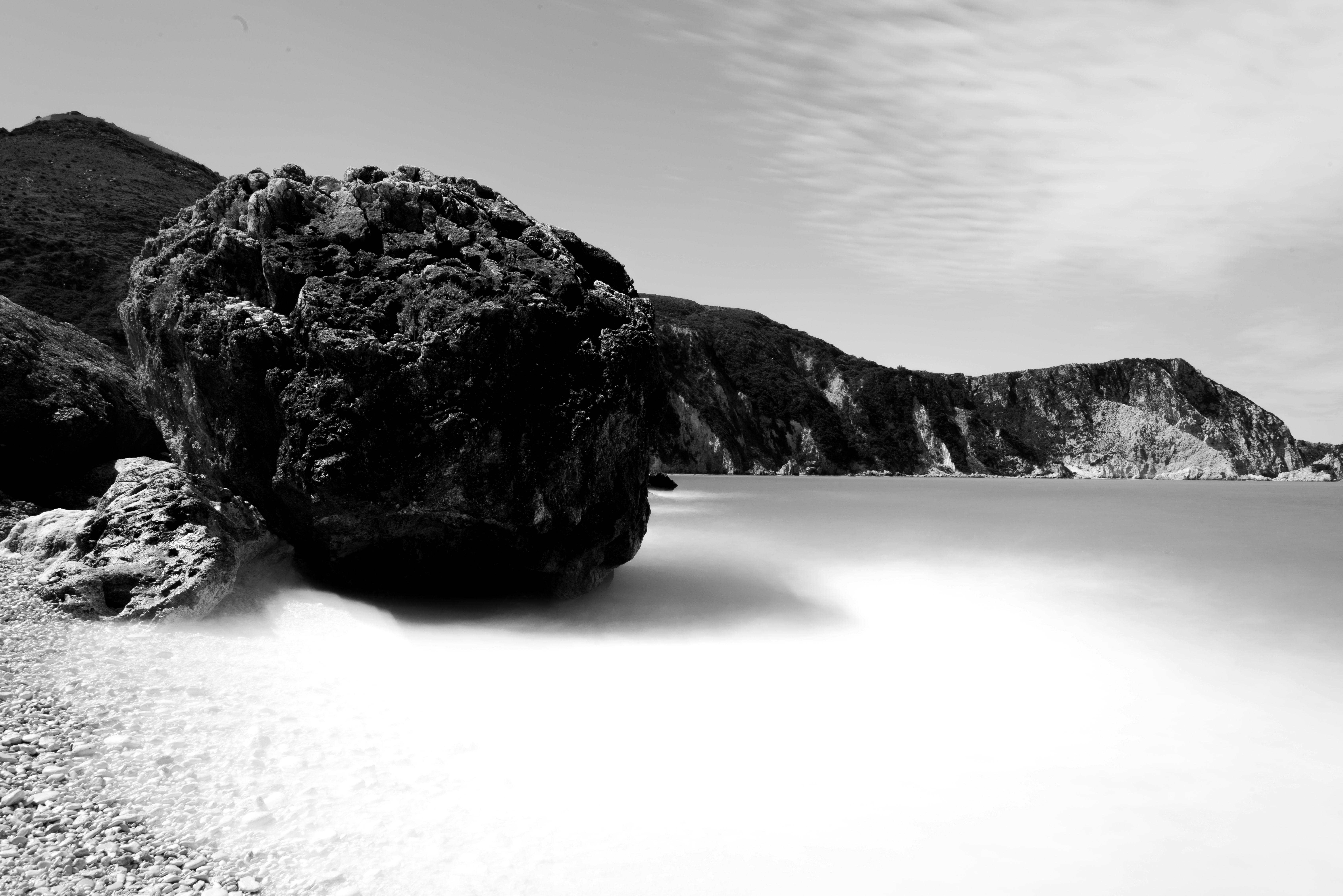 grayscale photo of coastline surrounded with rocky cliffs