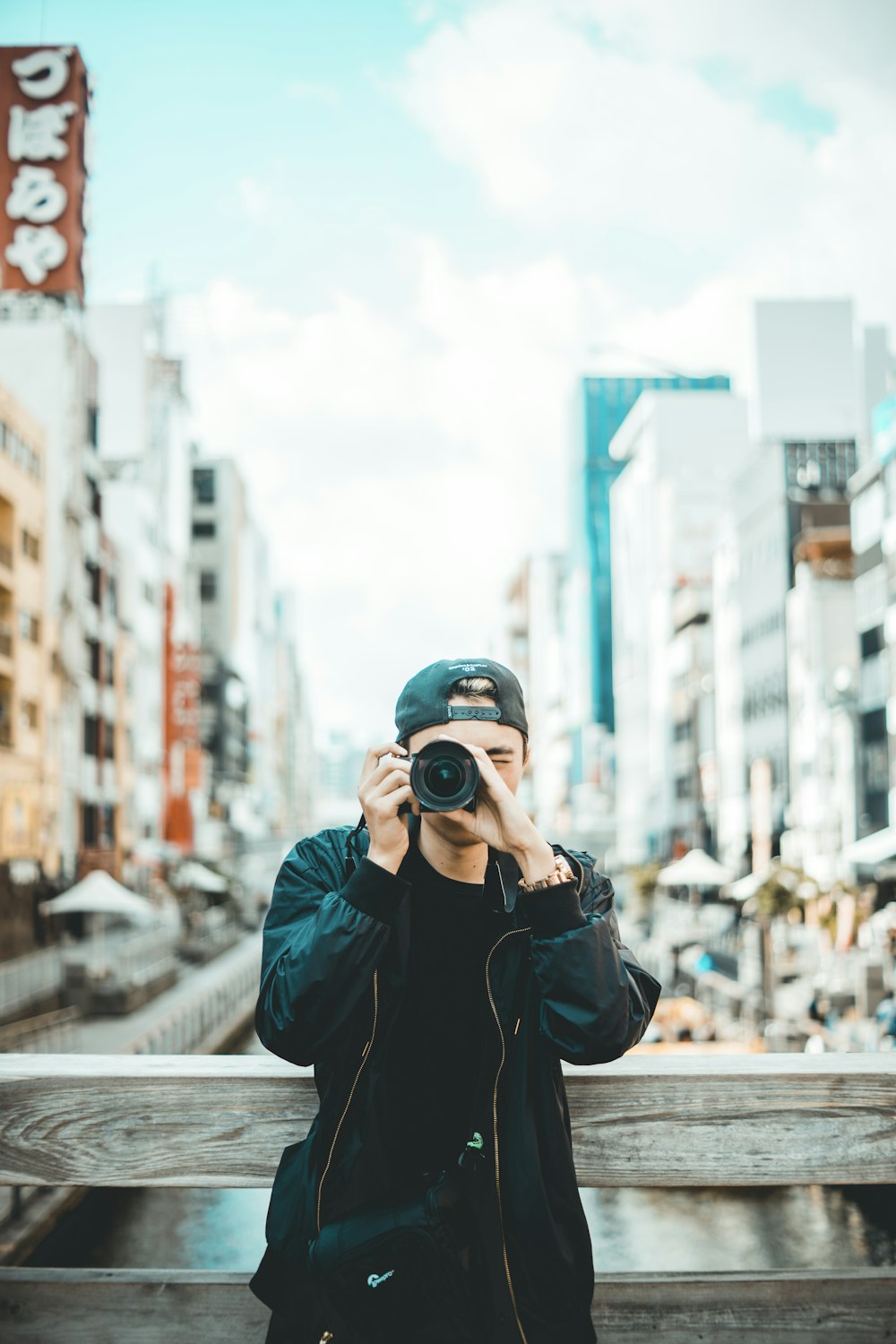 man wearing black jacket and cap holding DSLR camera during daytime