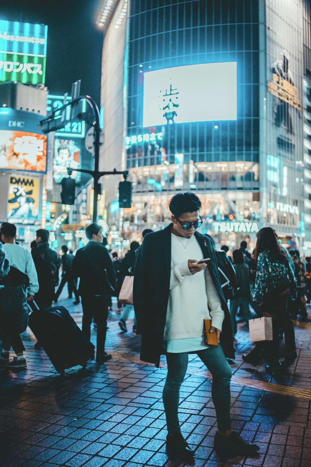 Hombre sosteniendo un teléfono inteligente parado frente a un edificio gris durante la noche