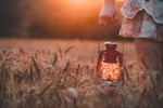 closeup photography of woman wearing floral skirt holding red gas lantern at brown grass field