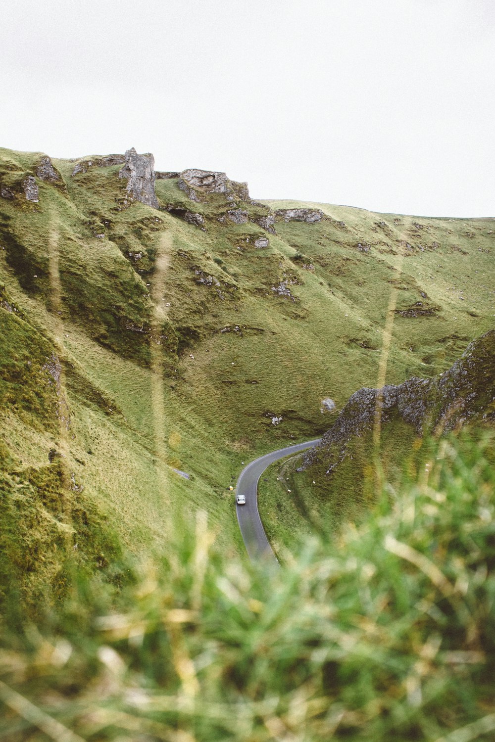 gray concrete road in between grass covered mountains