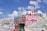 A colorful, artistic landscape with large words and religious messages painted on a hill. A group of people stands near the top beside a large cross. The phrases include 'God is Love' and 'Jesus I'm a Sinner.' The sky is clear with a few clouds.