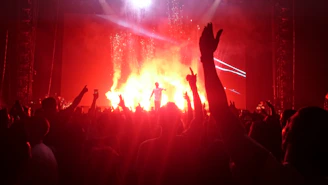 A vibrant concert scene bathed in striking orange lights with a young Ugandan artist passionately performing to an energetic crowd.