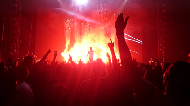 A vibrant concert scene bathed in striking orange lights with a young Ugandan artist passionately performing to an energetic crowd.