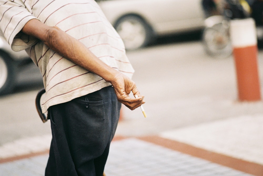 tilt-shift lens photography of man holding stick of cigarette during daytime