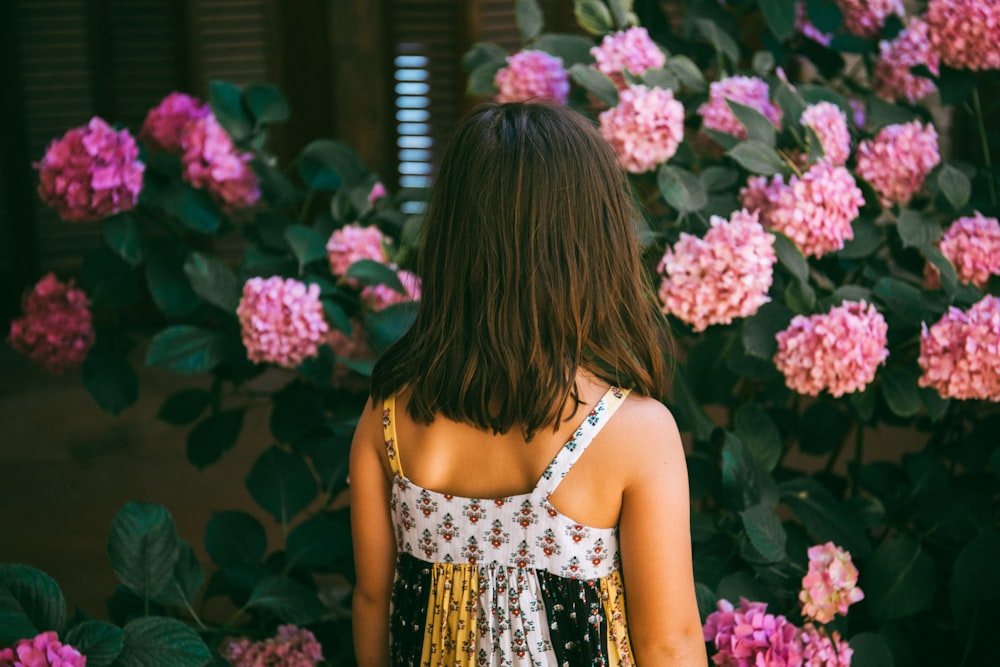 woman wearing white and multicolored floral-print sleeveless dress near pink flowers during daytime