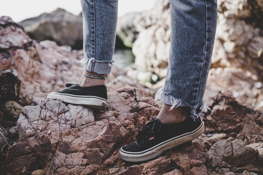 person wearing blue denim jeans and low-top sneakers standing on rock