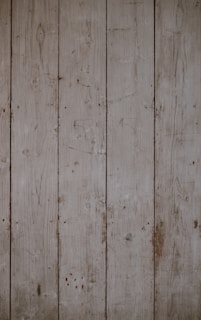 Weathered wooden planks aligned vertically with visible grains and knots, displaying a rustic and aged appearance.