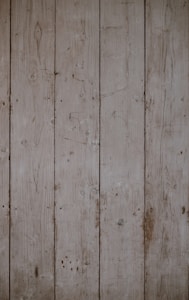 Weathered wooden planks aligned vertically with visible grains and knots, displaying a rustic and aged appearance.
