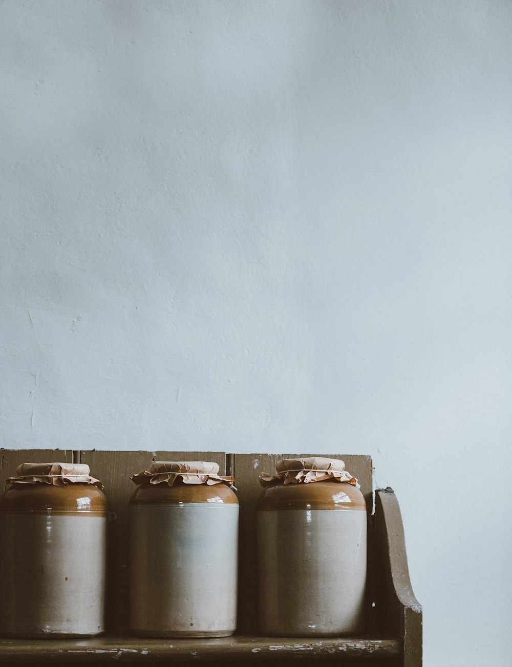 three white-and-brown ceramic jars on brown wooden rack