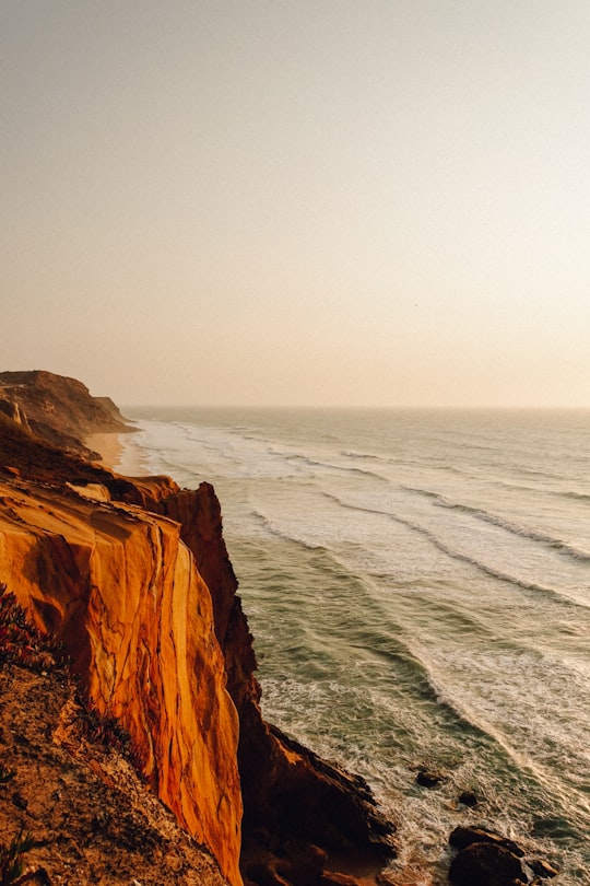 brown and black rock cliff beside ocean water during daytime in Santa Cruz Portugal