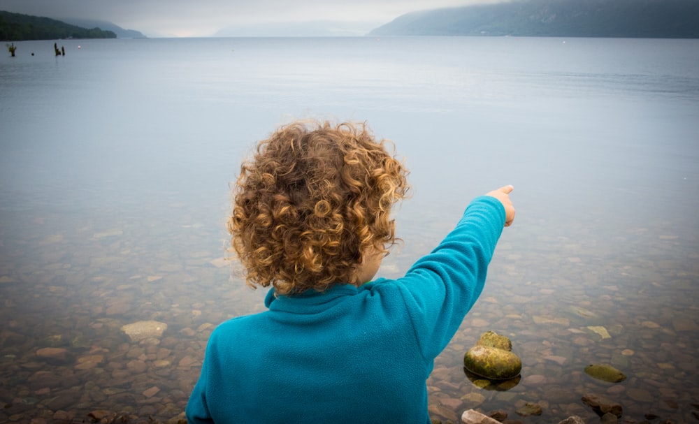 boy in blue turtleneck sweater pointing his finger on water