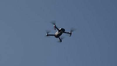 An instructor demonstrating drone operation to students outdoors with clear skies.