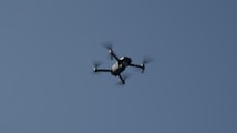A quadcopter drone flying in a clear blue sky with its propellers visibly spinning.