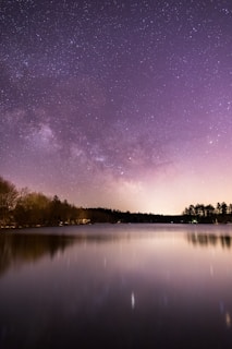 calm body of water overlooking trees under milky way