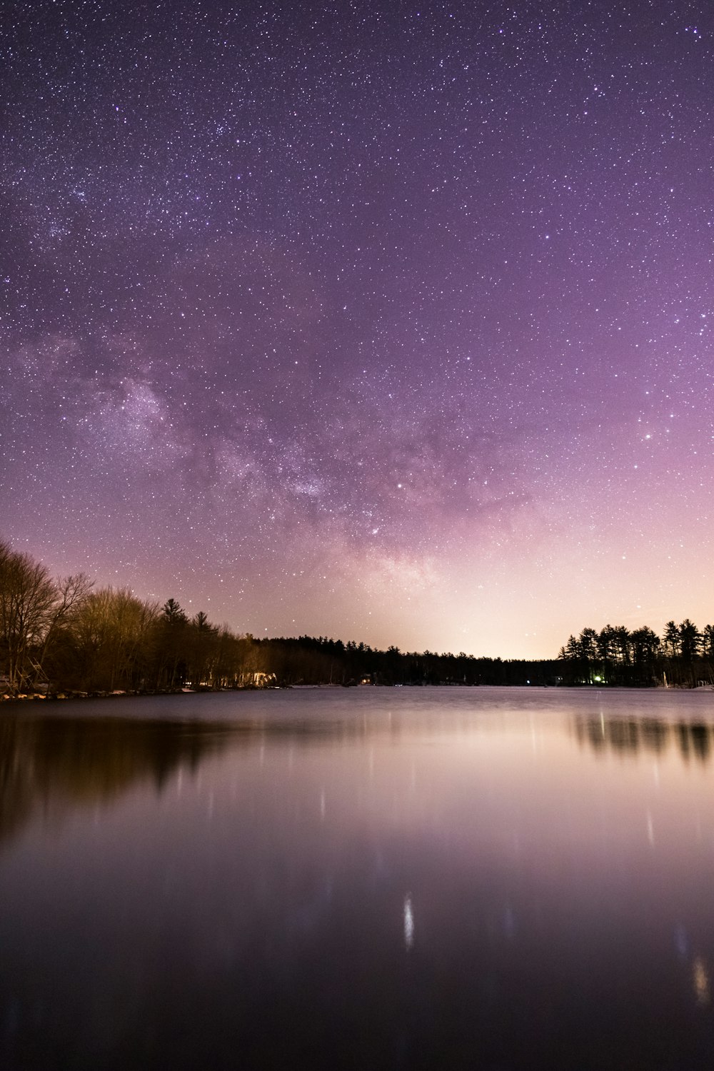 calm body of water overlooking trees under milky way