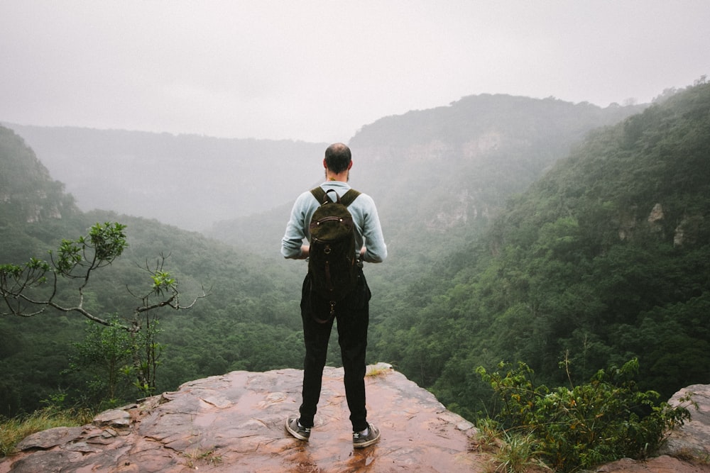man standing near cliff overlook mountains
