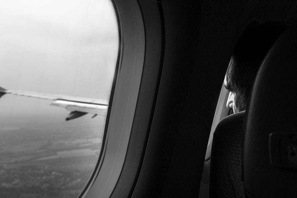 grayscale photo of man sitting near airliner window