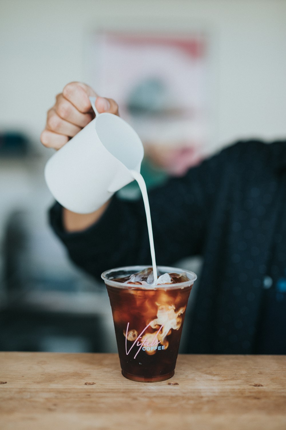 Fotografia de foco seletivo de pessoa segurando caneca derramando creme em copo plástico