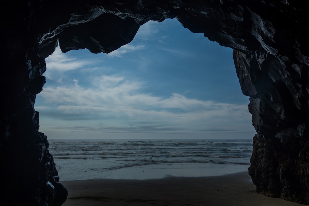 body of water under blue sky during daytime, Some Views are Better than Others.<p></figure>Walking along the beach on the Oregon Coast and came across this empty cave.