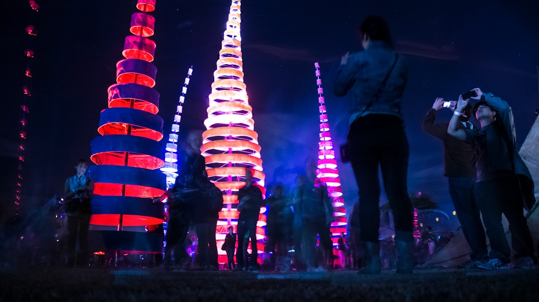 group of people standing beside four assorted-color lighted towers