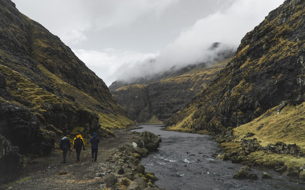 three person walking near river