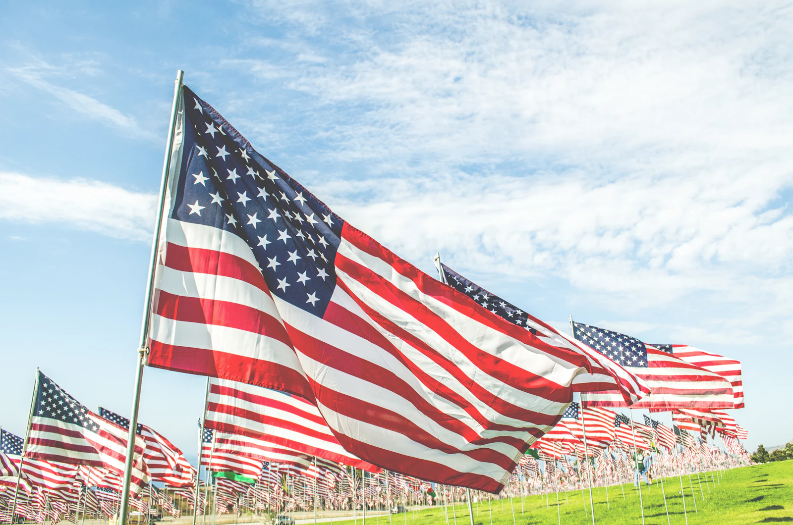 Rows of small American flags placed in a green field on a clear day for Memorial Day remembrance
