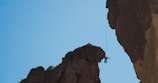 Dynamic shot of a climber leaping between two rock formations under a clear sky.