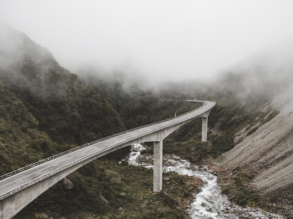 concrete bridge near mountains surrounded by fog