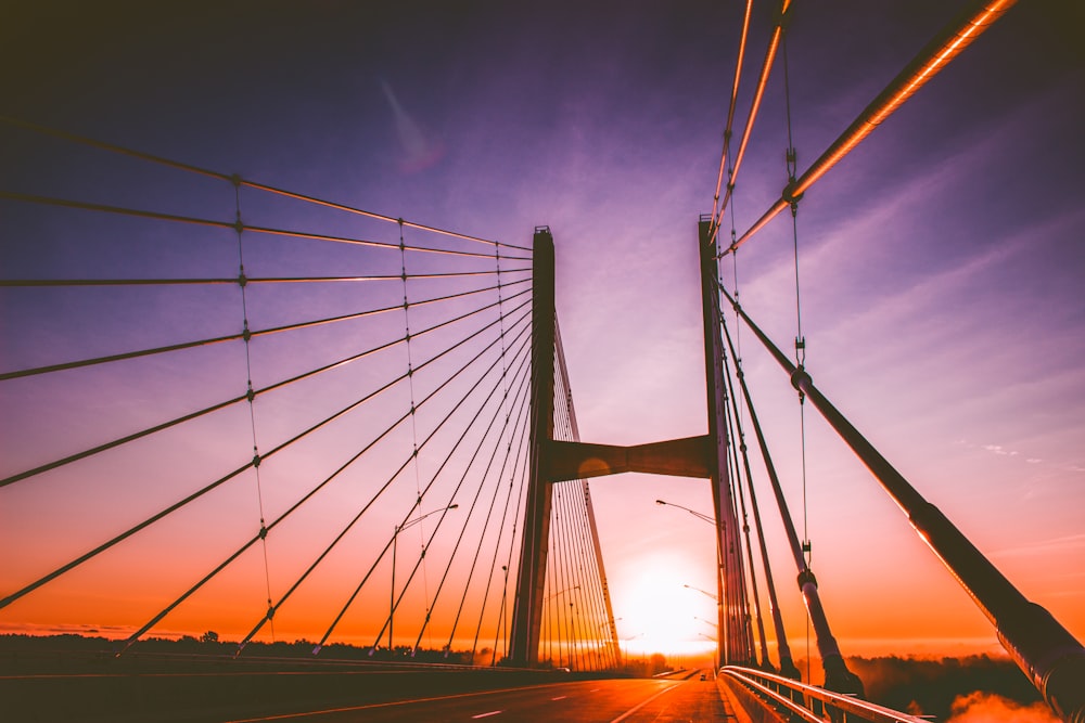 the sun is setting behind a bridge