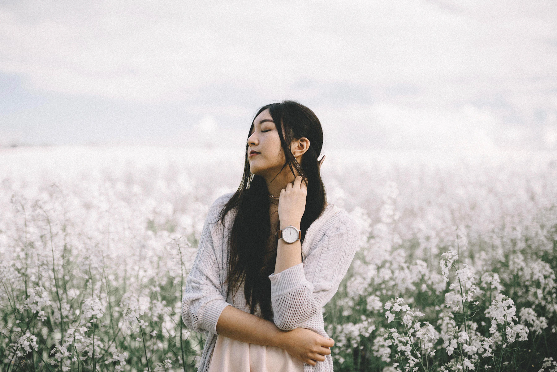 Woman in a white knit cardigan standing in a field of white blossoms