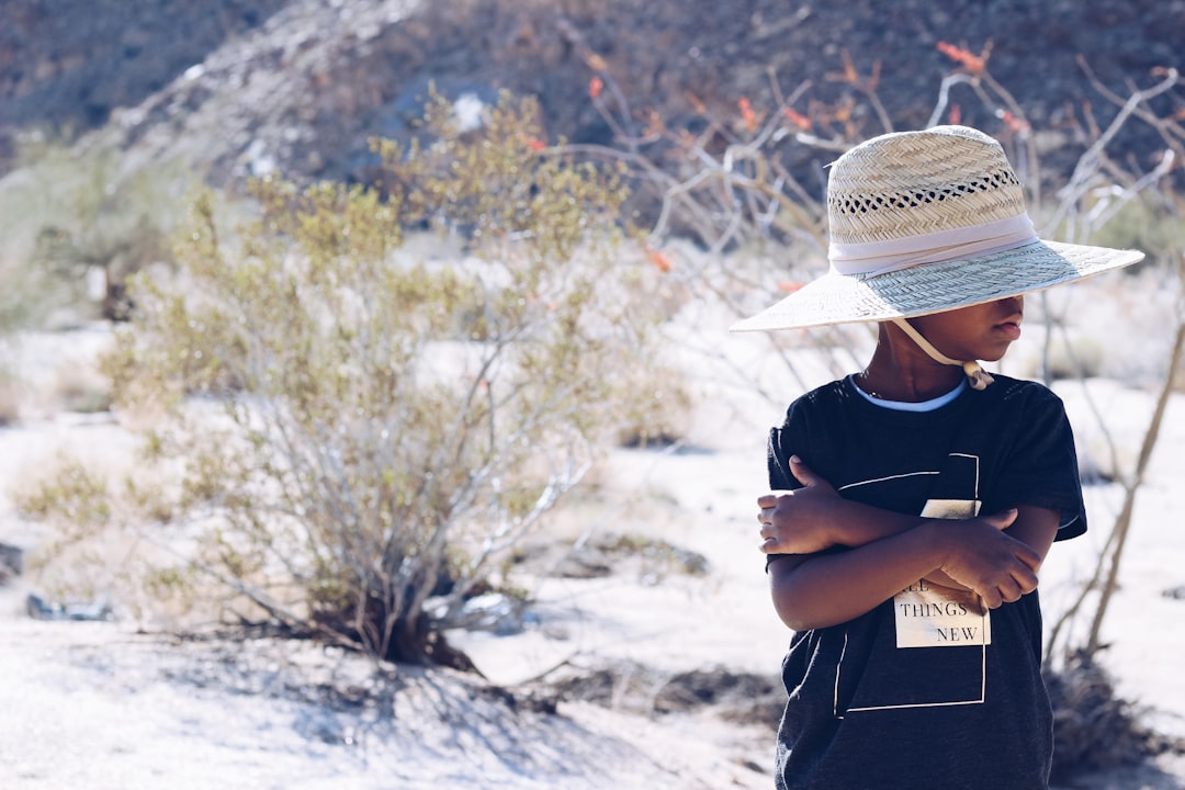 boy wearing black shirt and white hat standing beside green leafed plant