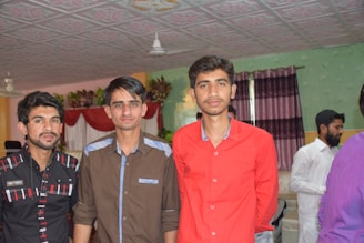 A group of young men sharing a supportive conversation in a cozy, modern room with dark blue walls and yellow accents.