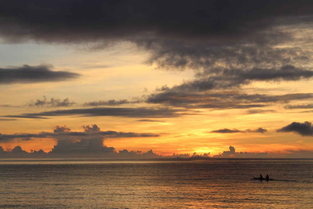 Photographie de silhouette de deux personnes équitation bateau au milieu de l’océan