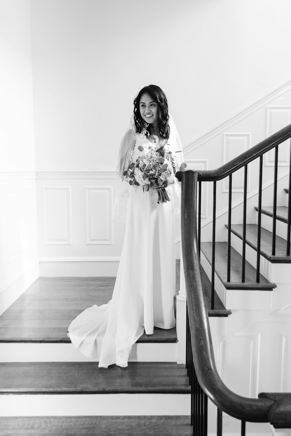 grayscale photo of woman standing on stairs in wearing dress and smiling