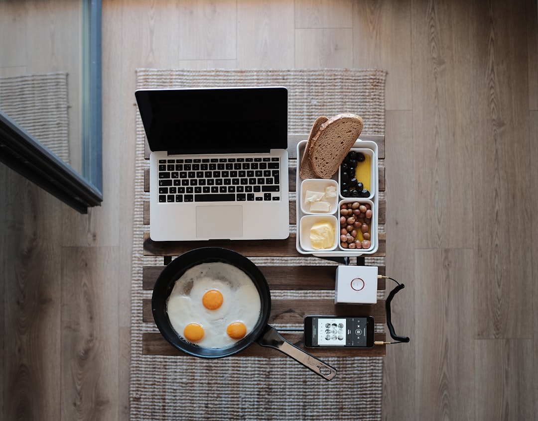 photo of MacBook Pro, frying pan with eggs and bread on gray mat
