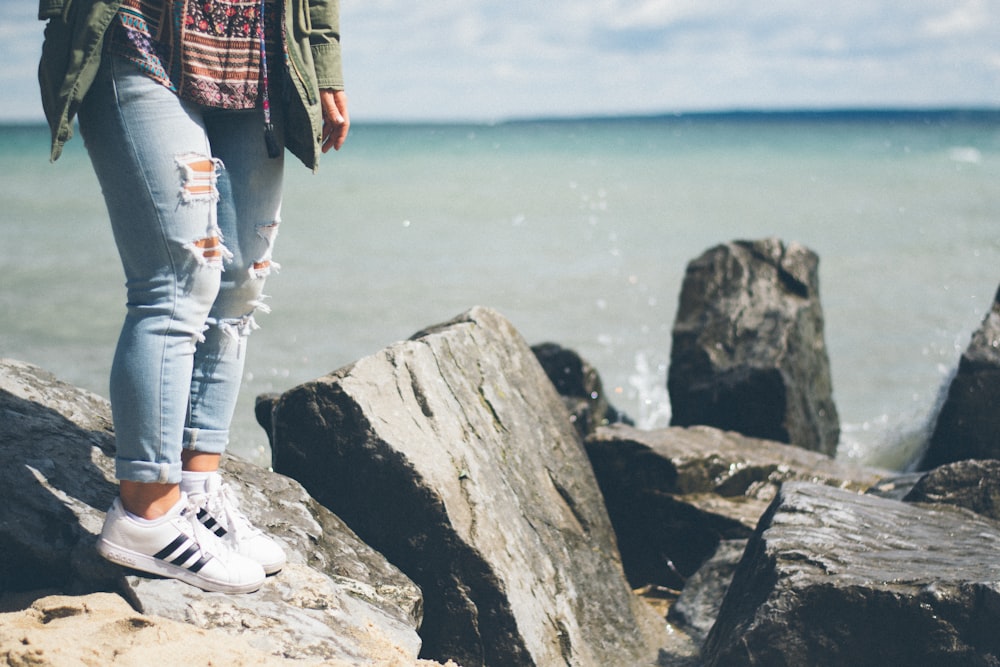 person standing on gray rock beside body of water